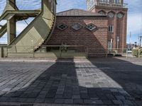 the shadow of a person standing in front of a tower near a brick building with a green staircase