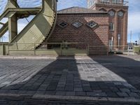 the shadow of a person standing in front of a tower near a brick building with a green staircase