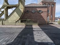 the shadow of a person standing in front of a tower near a brick building with a green staircase