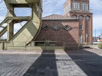 the shadow of a person standing in front of a tower near a brick building with a green staircase