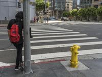 a person with a backpack standing at the corner of an intersection crossing the street near a yellow fire hydrant