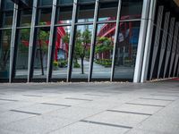 a person holding an umbrella walks in front of a glass building with a clock on it