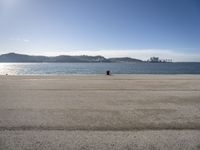 a person is sitting in the shade while waiting for a kite to fly over the water