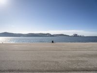 a person is sitting in the shade while waiting for a kite to fly over the water