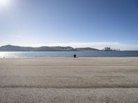 a person is sitting in the shade while waiting for a kite to fly over the water