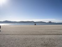 a person is sitting in the shade while waiting for a kite to fly over the water