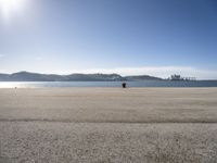 a person is sitting in the shade while waiting for a kite to fly over the water