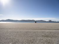 a person is sitting in the shade while waiting for a kite to fly over the water