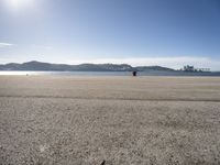 a person is sitting in the shade while waiting for a kite to fly over the water