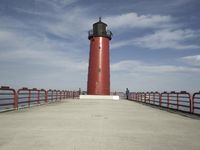 a person walks on a pier toward a light house, with the ocean in the background