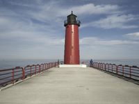 a person walks on a pier toward a light house, with the ocean in the background