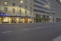 a city street lined with tall buildings in the evening hours with traffic passing by and oncoming, cars drive past and driving in front