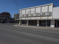 a view of a store called pianos on a street corner with parked cars in the background