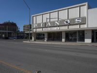 a view of a store called pianos on a street corner with parked cars in the background