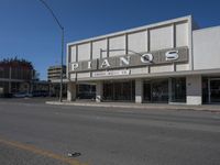 a view of a store called pianos on a street corner with parked cars in the background