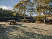 a picnic table sits on the grass by a lake with trees in the background and a walkway in the distance