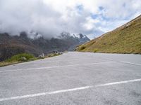 an empty road near the mountains with white markings in the road and snow capped hills on top