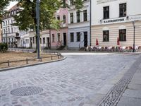 a cobblestone road leads through the middle of town where several people are eating outside a restaurant