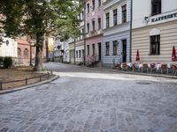 a cobblestone road leads through the middle of town where several people are eating outside a restaurant