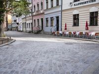 a cobblestone road leads through the middle of town where several people are eating outside a restaurant