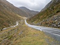 a winding country road through mountains and valleys below snow - capped peaks, a single passenger car is on the opposite side, and one person is on the right