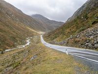 a winding country road through mountains and valleys below snow - capped peaks, a single passenger car is on the opposite side, and one person is on the right