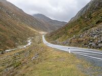 a winding country road through mountains and valleys below snow - capped peaks, a single passenger car is on the opposite side, and one person is on the right