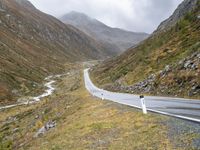 a winding country road through mountains and valleys below snow - capped peaks, a single passenger car is on the opposite side, and one person is on the right