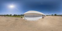 a fish eye picture of a horse barn, with dirt ground and blue sky in the background