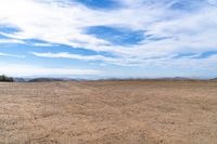 an empty dirt field and sky with clouds above it and blue skies overhead with mountains and blue sky