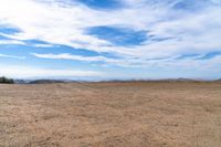 an empty dirt field and sky with clouds above it and blue skies overhead with mountains and blue sky