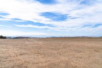 an empty dirt field and sky with clouds above it and blue skies overhead with mountains and blue sky