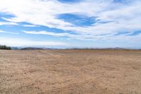 an empty dirt field and sky with clouds above it and blue skies overhead with mountains and blue sky