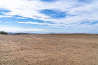 an empty dirt field and sky with clouds above it and blue skies overhead with mountains and blue sky