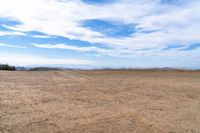 an empty dirt field and sky with clouds above it and blue skies overhead with mountains and blue sky