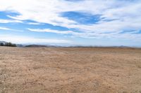 an empty dirt field and sky with clouds above it and blue skies overhead with mountains and blue sky