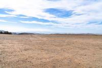 an empty dirt field and sky with clouds above it and blue skies overhead with mountains and blue sky