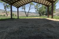 a barn with lots of hay in it and mountains in the distance above the buildings