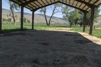 a barn with lots of hay in it and mountains in the distance above the buildings