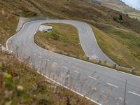 a car drives down a curvy mountain road next to a forest covered hill