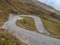 a car drives down a curvy mountain road next to a forest covered hill