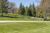 a wooden fence in a green field of grass near trees and flowers on the side of the road