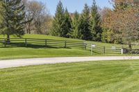 a wooden fence in a green field of grass near trees and flowers on the side of the road