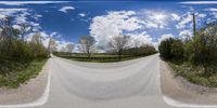 a 360 - view view shows an empty country road with trees and fences on the other side of the road