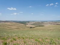 a hilly plain with rolling hills and valleys in the distance, blue skies in the distance