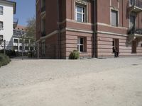 the view from behind the fence looking down at a building, featuring a small man walking across a driveway