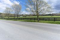 a country road with the fence off to the side of it and grass to the right