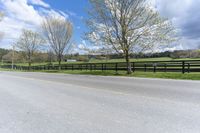 a country road with the fence off to the side of it and grass to the right