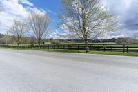 a country road with the fence off to the side of it and grass to the right