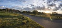 a paved road with grass in the foreground and a house and house on the hill in the distance